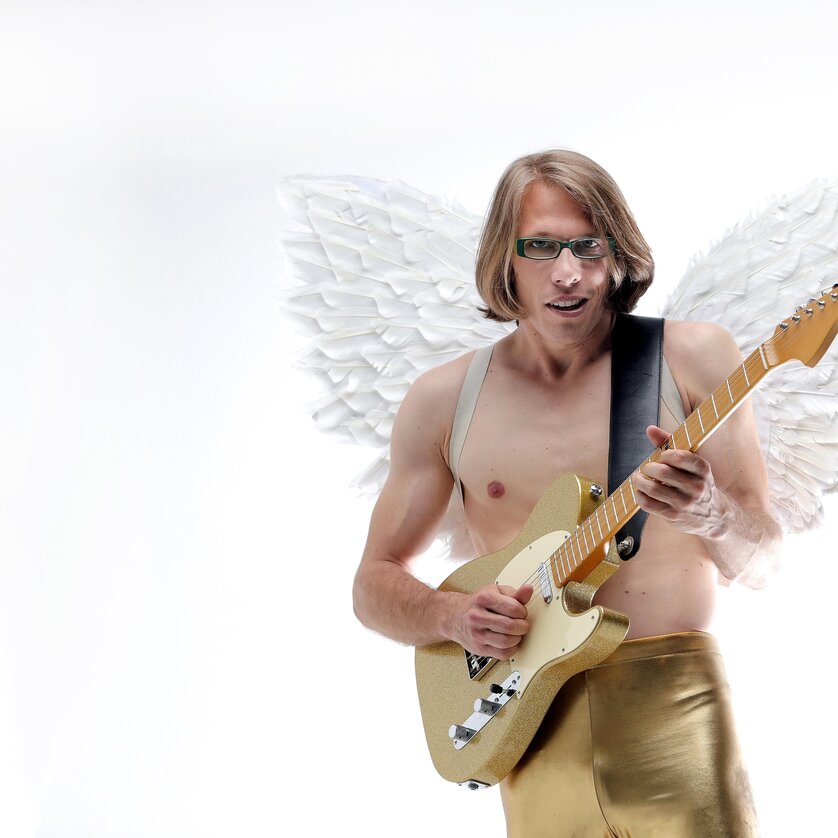 Mann mit Flügeln spielt Gitarre in goldenen Hosen. | © Volker Weihbold