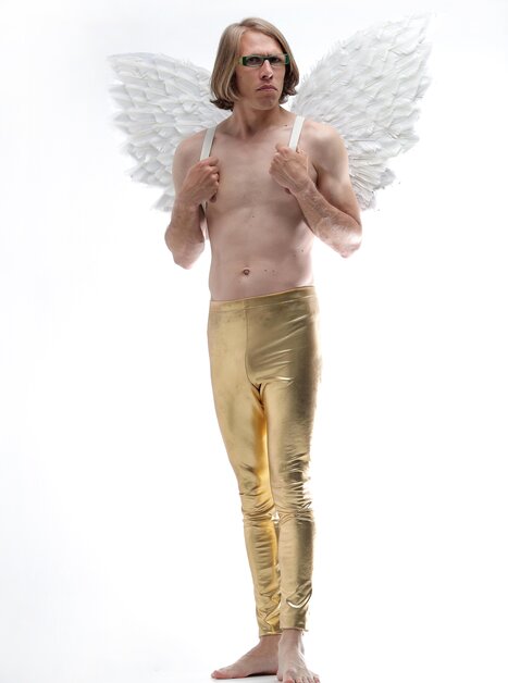 Ein Mann trägt Engelsflügel und goldene Leggings, steht barfuß und posiert. | © Volker Weihbold