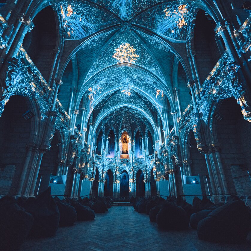 Illuminated, ornate cathedral with bean bags in the foreground. | © Projektil