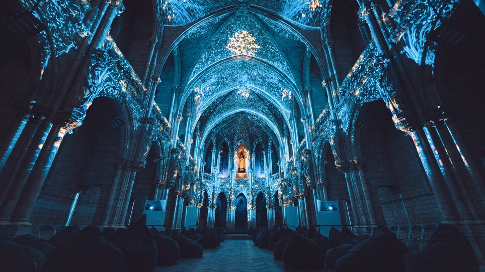 Beleuchtete, verzierte Kathedrale mit Sitzkissen im Vordergrund. | © Projektil