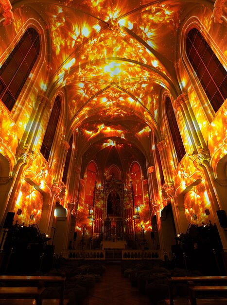 Ein Kircheninneres, lebhaft erleuchtet von warmen Lichtmustern. | © Projektil