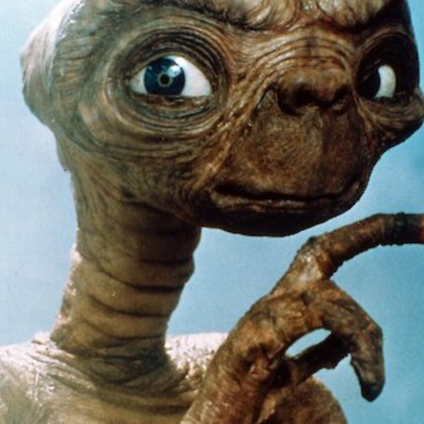 An alien creature with big eyes and a glowing finger shows curiosity. | © Universal City Studios, Inc.