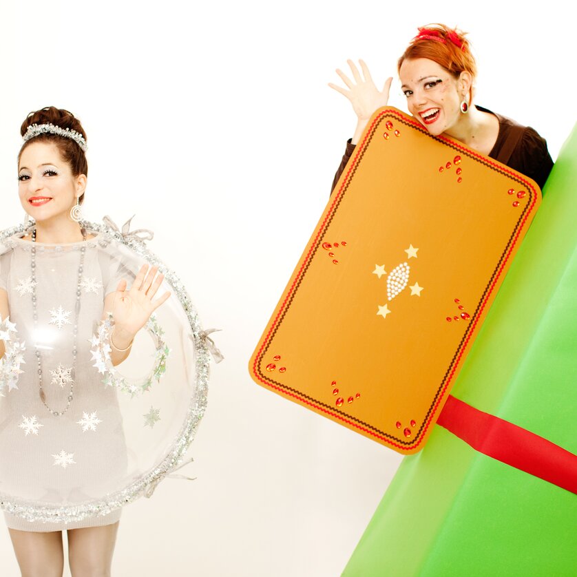 Zwei Frauen in kreativer Weihnachtskleidung, eine als Geschenk und die andere als Schneekugel. | © Julia Wesely