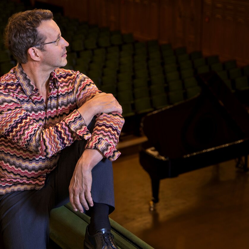 Ein Mann sitzt in einem Konzertsaal neben einem Klavier. | © PILO PICHLER