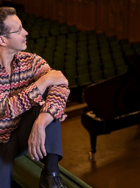 Ein Mann sitzt in einem Konzertsaal neben einem Klavier. | © PILO PICHLER