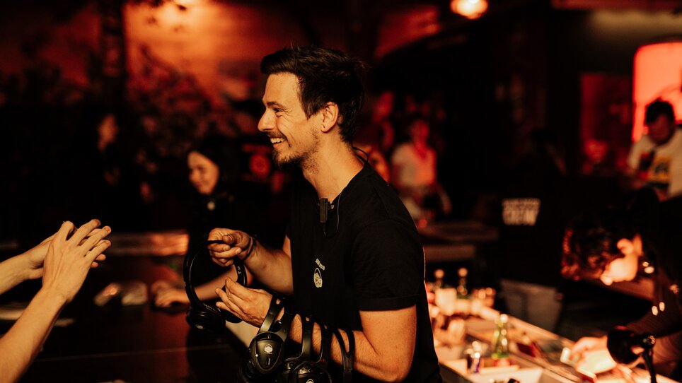 Lächelnder Mann mit Kopfhörern in einem lebhaften Veranstaltungsraum bei einer Silent Disco. | © Silent Disco Austria