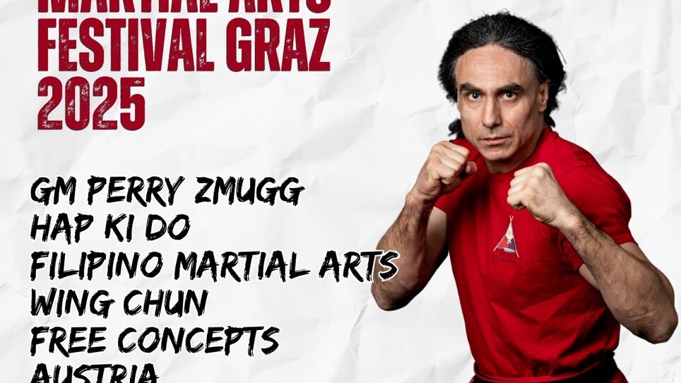 Meister Perry Zmugg posiert mit geballten Fäusten und blickt konzentriert in die Kamera, er trägt ein rot-schwarzes Kampfsport-Outfit. | © Körper Kampf Kunst Center Zmugg
