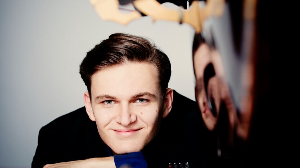 Portrait von Dominik Wagner mit lächelndem Gesicht, lehnt am Klavier. | © Julia Wesely