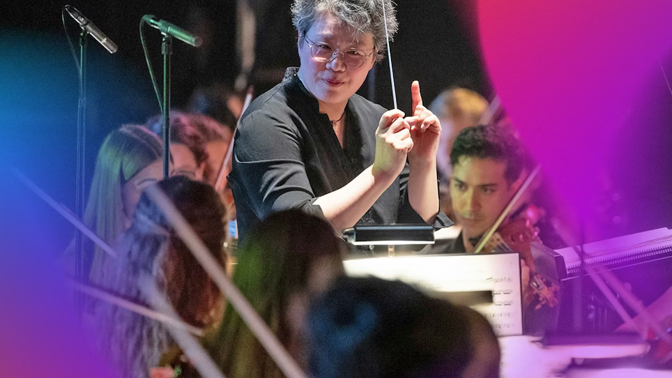 Dirigentin Mei-Ann Chen steht vor einem Orchester und dirigiert leidenschaftlich. | © Milatovic