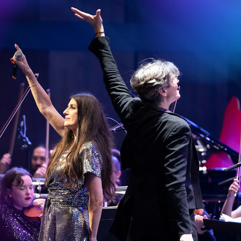 Two artists raise their hands in the spotlight during a concert. | © Milatovic