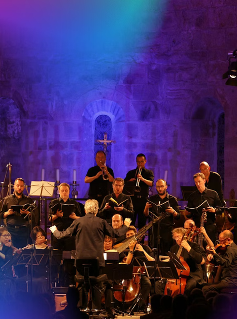 An orchestra performs under a conductor in an illuminated church. | © pouyfourcat