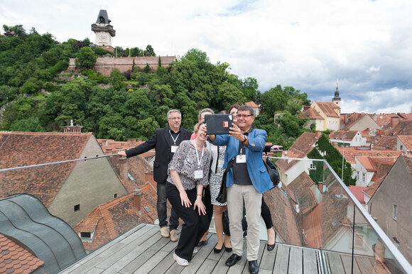 Gruppe von fünf Personen posiert auf Dachterrasse mit Blick auf Graz und den Uhrturm.