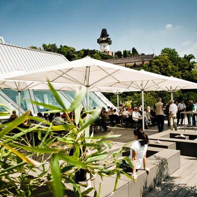 Dachterrasse mit Gästen, Blick auf den Grazer Uhrturm und die Stadt Graz.
