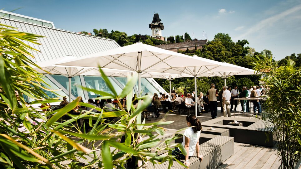 Rooftop terrace with guests, view of the Graz Clock Tower and the city.
