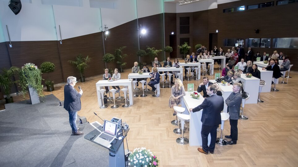 A conference with many attendees in a modern room with a bar and plants. | © MCG - Martin Wiesner