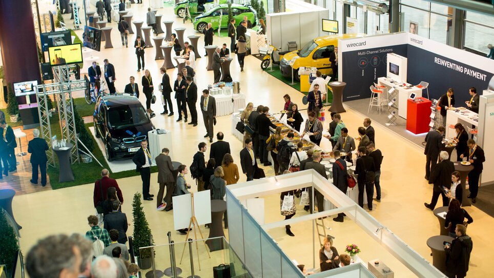 View of a conference with attendees, booths, and vehicles at an exhibition | © MCG - Martin Wiesner