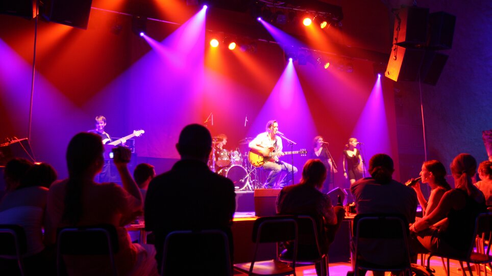 Eine Band spielt live auf der Bühne im Dom im Berg mit bunten Lichtern. | © Graz Tourismus - Harry Schiffer
