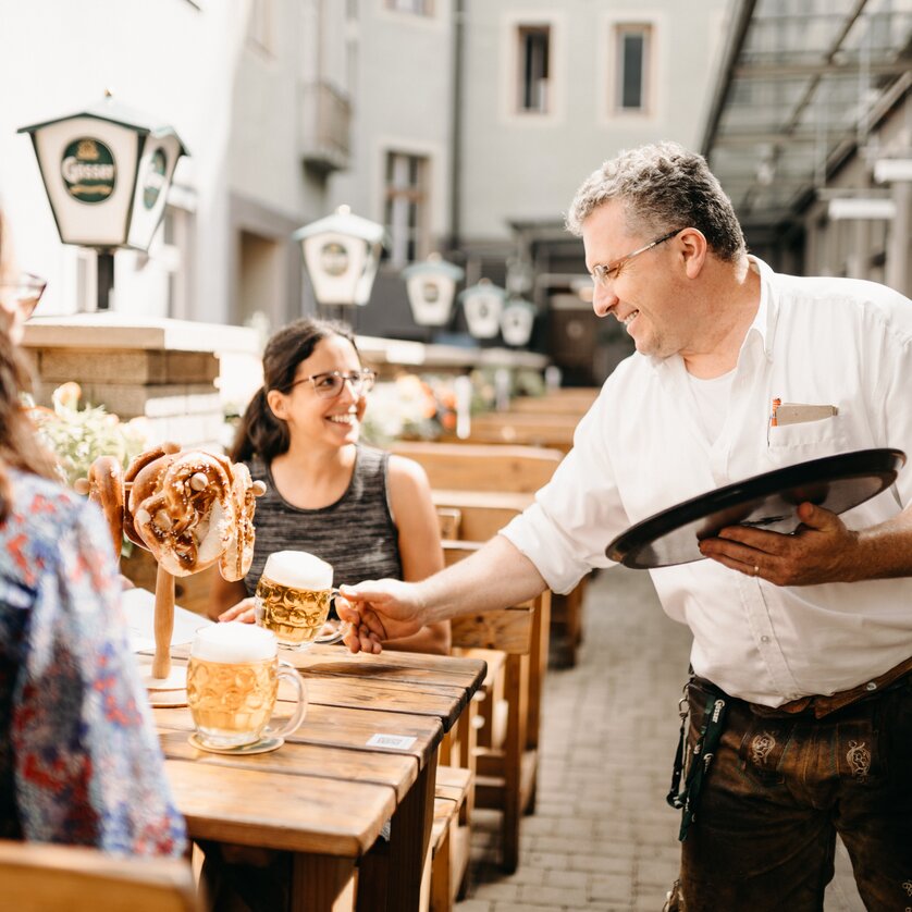 A waiter serving beer and pretzels to customers in the garden of Gösserbräu restaurant. | © glddggrs-35