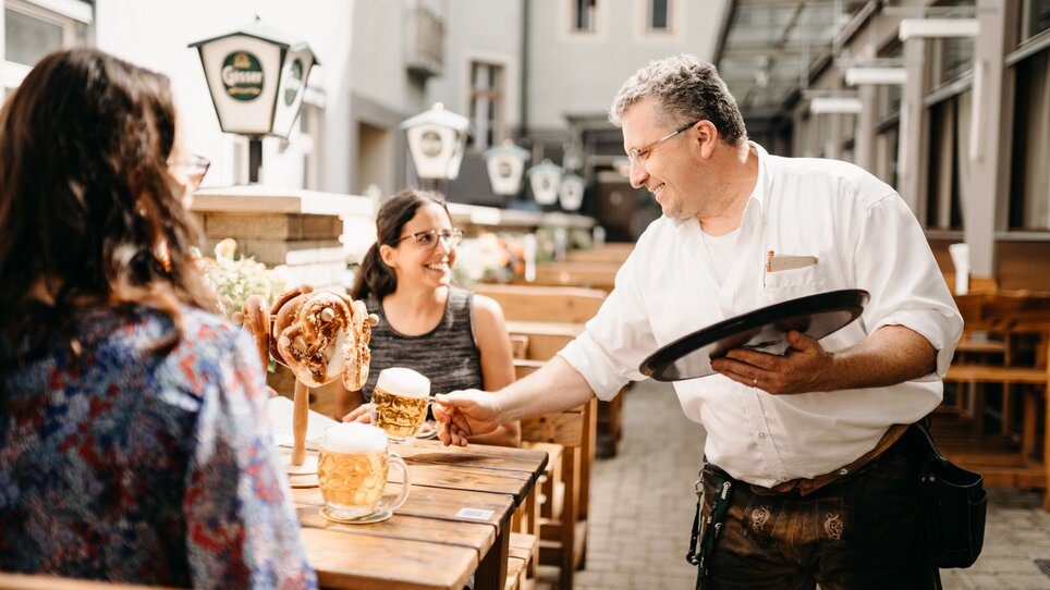Ein Kellner serviert Bier und Brezeln an Kunden im Garten des Gösserbräu Restaurants. | © glddggrs-35