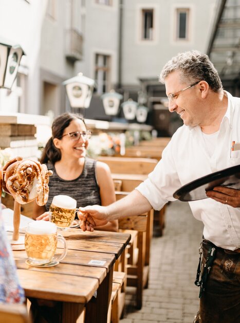 Ein Kellner serviert Bier und Brezeln an Kunden im Garten des Gösserbräu Restaurants. | © glddggrs-35