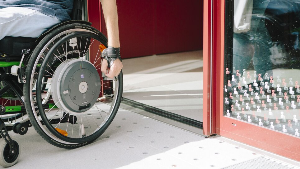 Person in a wheelchair opening a door with one hand. | © Sebastian Reiser