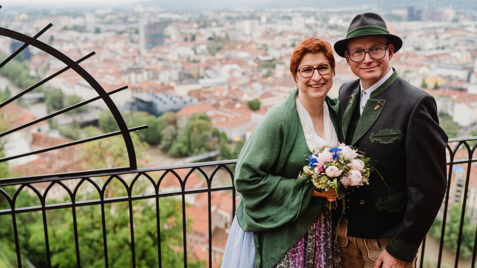 Wedding photo of a couple in front of Graz city with colorful flowers. | © Tom Schuller