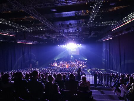 Orchestra performing in a dimly lit auditorium with audience. | © Helmut List Halle