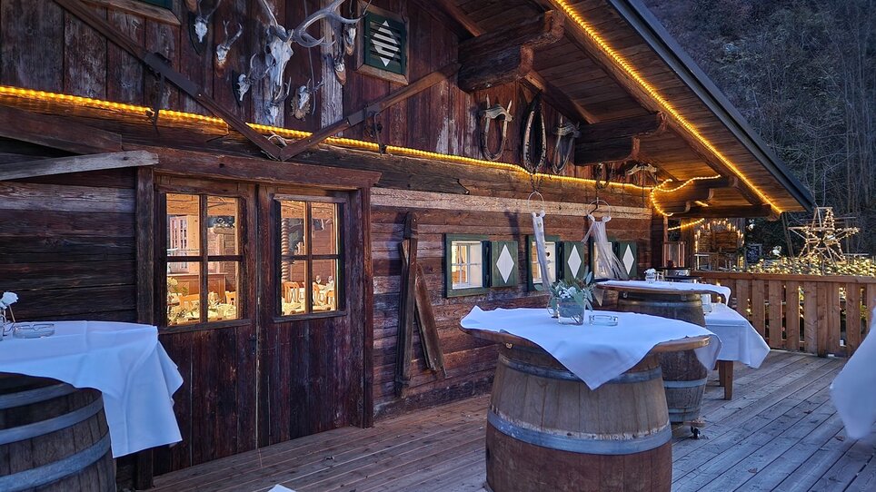 Außenansicht der Almhütte Graz mit Holzfassade und Tischen. | © I AM Hotels