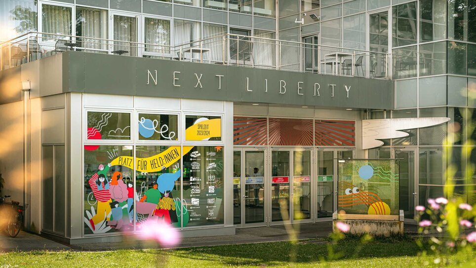 Das Next Liberty präsentiert moderne Architektur mit großen Fenstern und bunten Grafiken. Der Veranstaltungsort bietet eine helle Atmosphäre für Konferenzen und Networking. | © Stella
