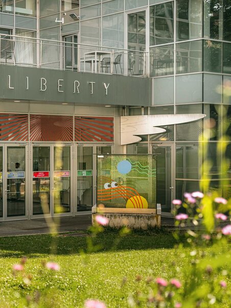 Das Next Liberty präsentiert moderne Architektur mit großen Fenstern und bunten Grafiken. Der Veranstaltungsort bietet eine helle Atmosphäre für Konferenzen und Networking. | © Stella