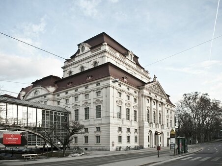 Teatro dell'Opera di Graz con facciata storica, ponte di vetro e fermata dell'autobus in una strada vuota | © Moodley Brand Identity