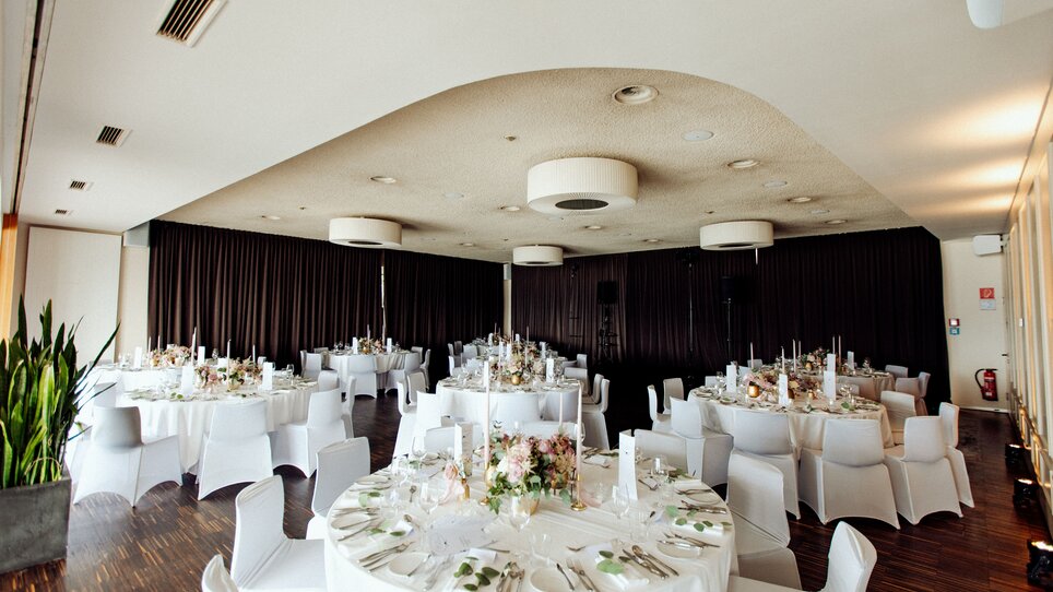 Elegante Meetinglocation mit runden Tischen, stilvoll dekoriert, großzügiger Raum mit guter Lichtausstattung, ideal für Veranstaltungen. | © Restaurant SCHLOSSBERG - Kyrillos Mikhail