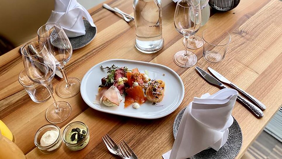 Im Schlossberg Restaurant sind ein elegant gedeckter Tisch und ein ansprechendes Essen mit Blick auf Graz zu sehen. Die moderne Atmosphäre und das stilvolle Ambiente bieten optimale Bedingungen für Business-Events und Tagungen. | © Restaurant Schlossberg