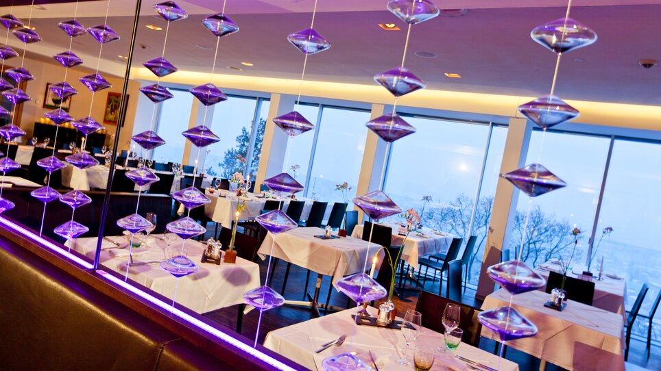 Moderne Innenausstattung mit Tischanordnung, großen Fenstern und Beleuchtung im Schlossberg Restaurant. Ideal für Konferenzen und Geschäftsmeetings. | © Schlossberg Restaurant