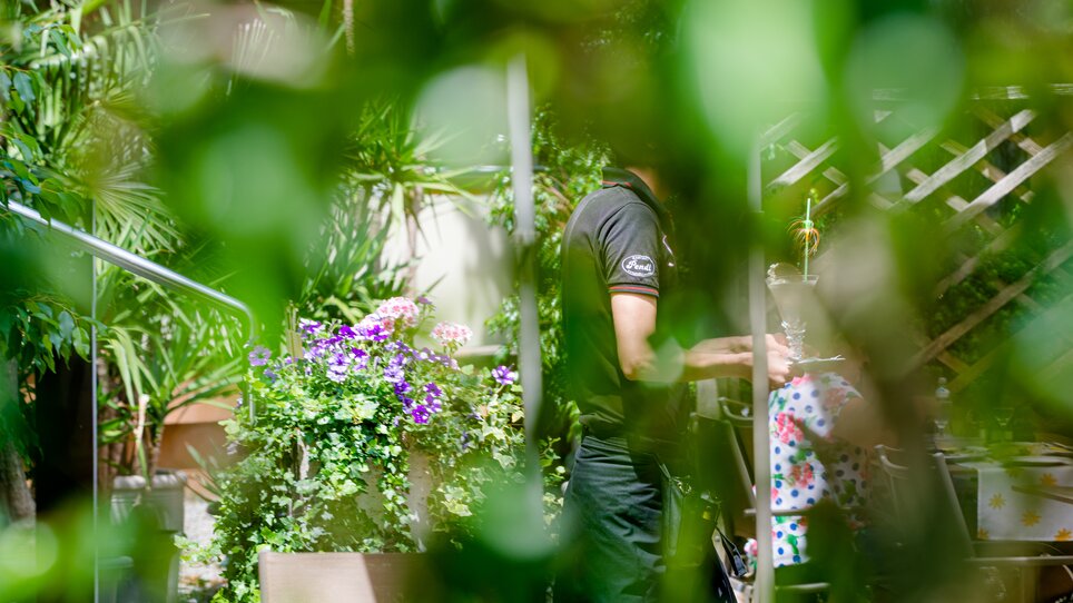 View of a serene garden landscape featuring blooming plants and people in the background at Hotel-Gasthof Pendl. | © Mias Photoart