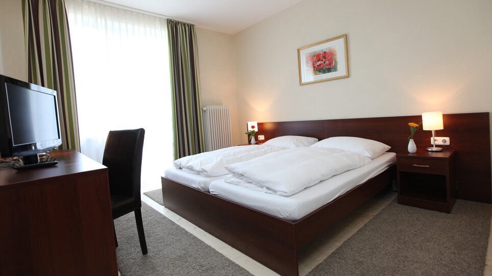 Ein Schlafzimmer im Hügellandhof mit zwei Betten, Fernseher und Fenster. | © Hügellandhof