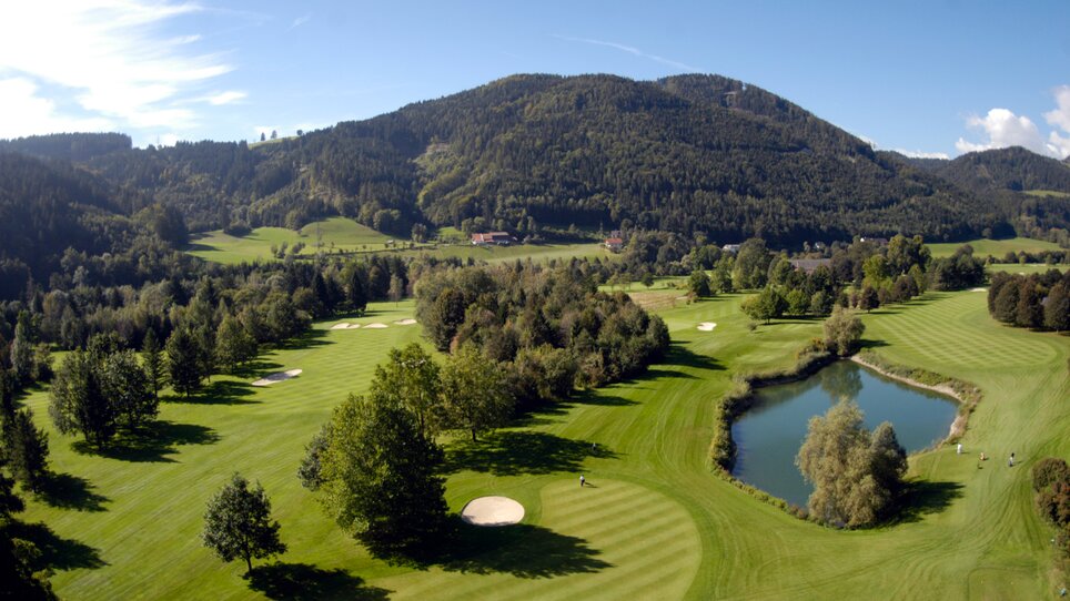 Panoramablick auf einen Golfplatz umgeben von Bergen und einem Teich in der Nähe des Murhof Hotel & Restaurant. | © Murhof