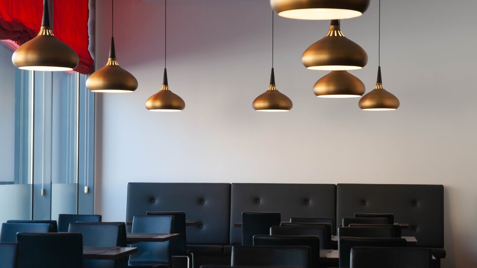 Helle, elegante Restaurantaufführung mit goldenen Lampen und schwarzen Möbeln im PLAZA INN Graz City. | © PLAZA INN Graz City