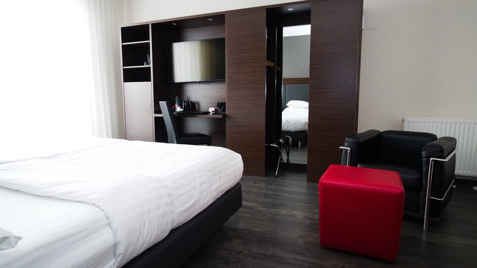 Ein stilvolles Hotelzimmer mit einem Bett, Arbeitsbereich und schwarzem Sessel im PLAZA INN Graz City. | © PLAZA INN Graz City