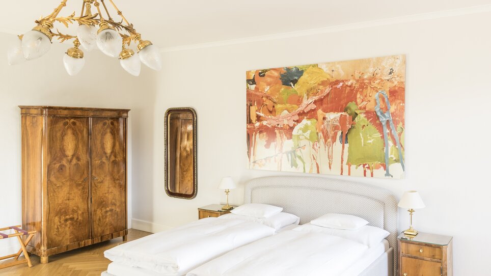 Helles Schlafzimmer im Schlossberghotel mit Holzschrank und abstrakter Malerei. | © Schlossberghotel