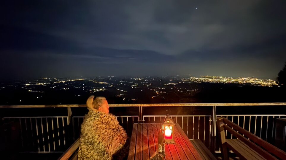 Person wrapped in a blanket with lantern, view of Graz city at night from Stubenberghaus. | © Stubenberghaus