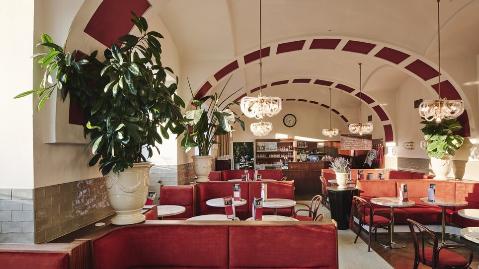 Interior view of a café in Hotel Das Weitzer with red upholstery, tables, and guests chatting. | © Florian Weitzer Hotels & Restaurants