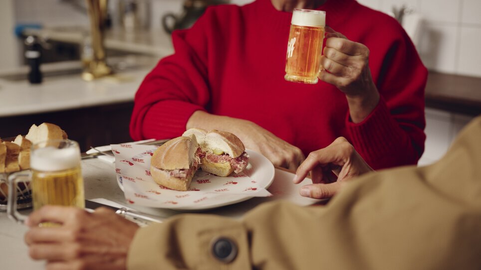 Im Restaurant des Hotel Weitzer hält eine Person ein Bier, während eine andere ein Sandwich genießt. | © Florian Weitzer Hotels & Restaurants (5) - Kopie