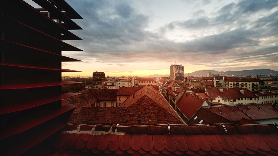 Panorama von Graz mit Dächern und Sonnenuntergang hinter Wolken. | © Florian Weitzer Hotels & Restaurants