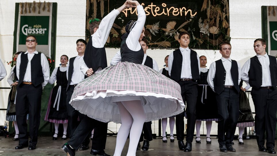 Tanzende Personen in traditioneller Kleidung auf einer Bühne. | © Ivents Kulturagentur