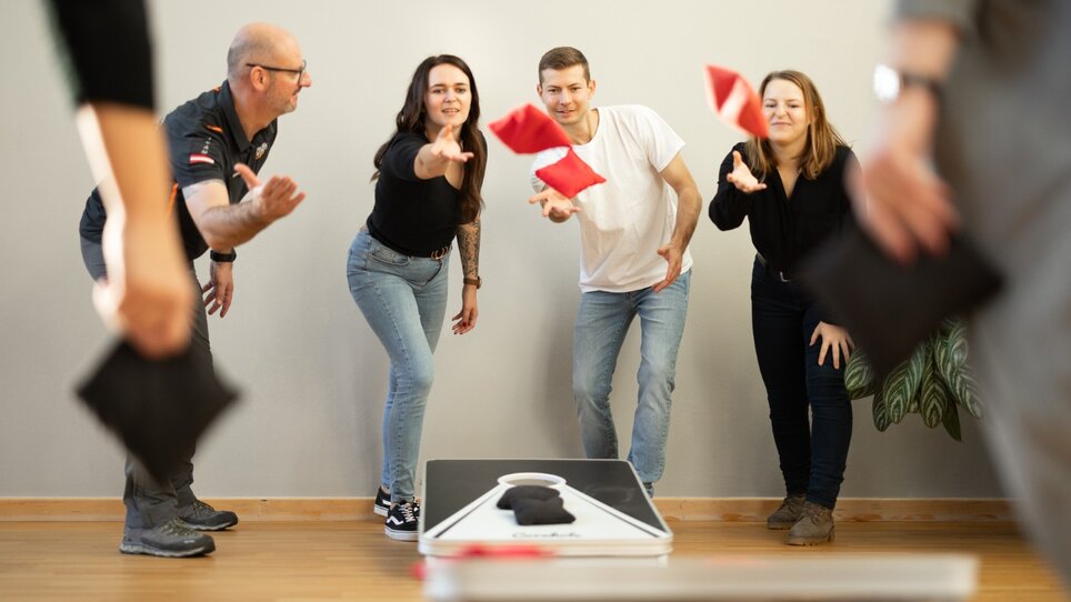 Vier Personen werfen Säckchen auf ein Spielbrett bei einem Teamspiel. | © Retter Events