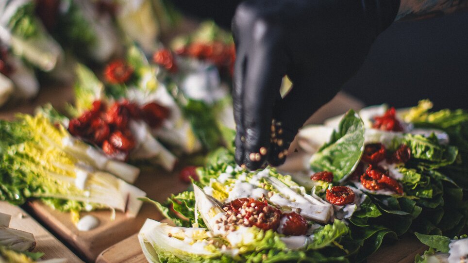 Fresh salad dishes are being prepared by chefs of the catering company The Underground Kitchen. A chef adds ingredients to the beautifully arranged salads. | © Alex Rauch