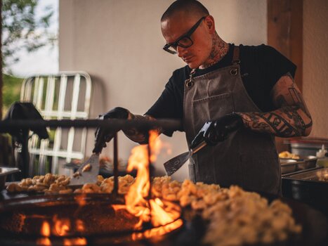 A chef of The Underground Kitchen // crew works focused at the grill with flames and prepared dishes in The Underground Kitchen //. | © Alex Rauch