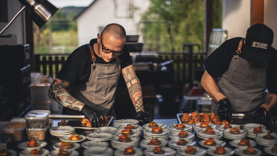 Two chefs garnishing plates in a kitchen with gourmet dishes. | © Alex Rauch