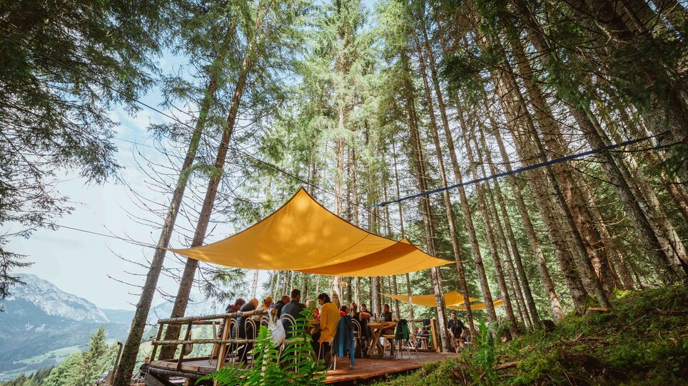 People gather under orange sunshades in the forest. | © Alex Rauch